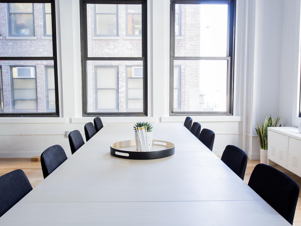 Sala de juntas vacía con mesa blanca, sillas oscuras y ventanales